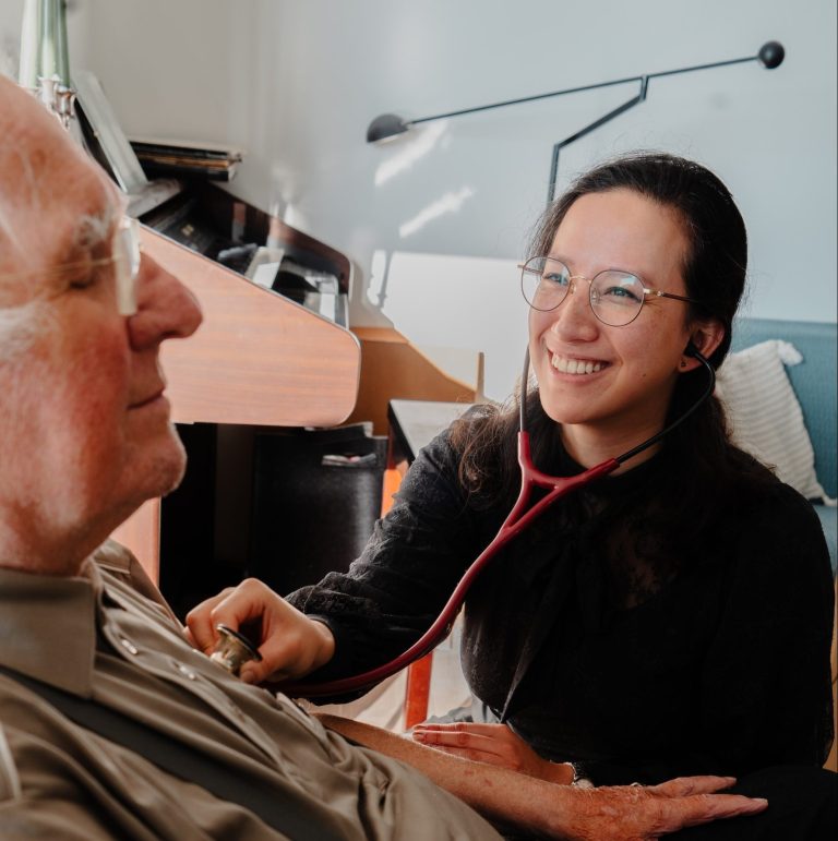 Jonge arts luistert hartslag bij oudere cliënt tijdens huisbezoek – Werken bij GeriCall